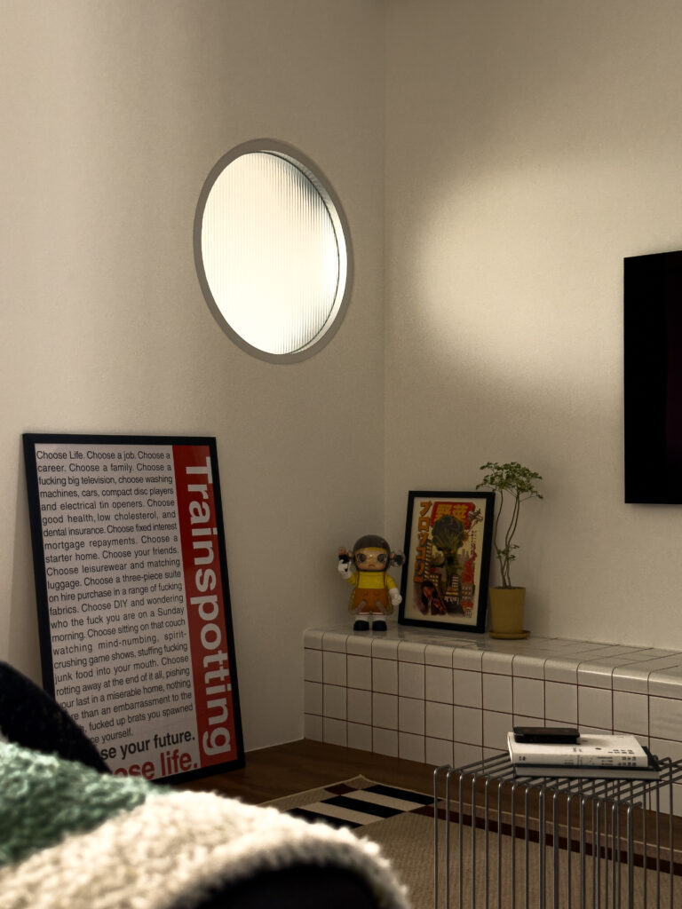 Detail shot of the circular fluted glass window beside the TV, with a Trainspotting poster, a toy figure, and a framed Japanese art print on the tiled ledge.
