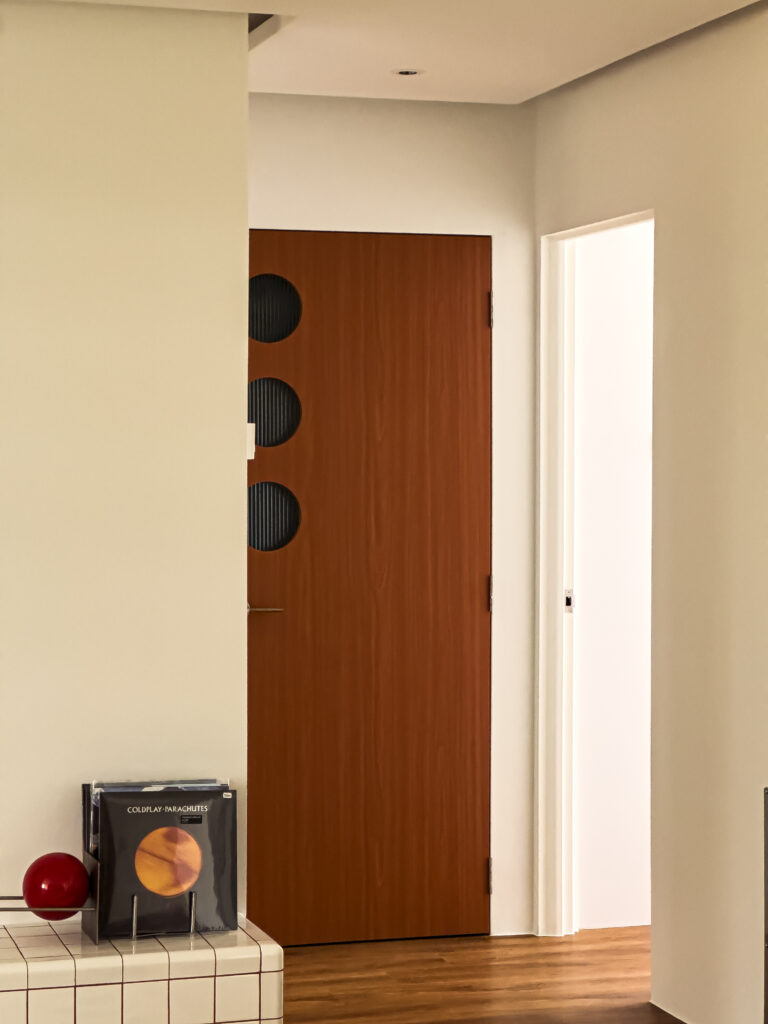 Close-up of a timber door featuring three circular fluted glass cut-outs, showing the grain of the wood and subtle reflection of natural light.