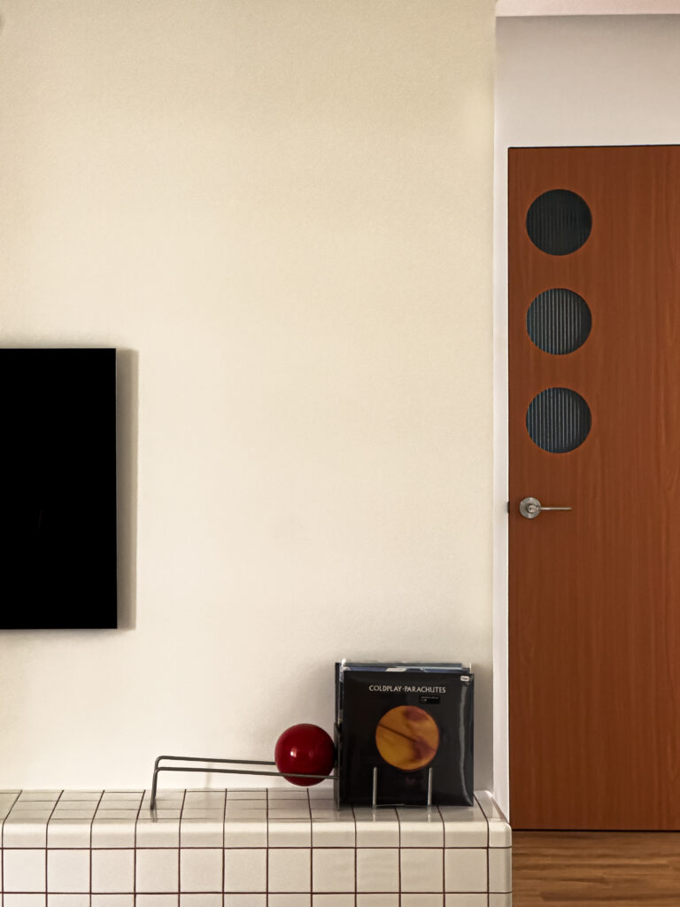 View of the tiled TV console with a Coldplay record and a red orb decor piece placed beside the wooden door, creating a balance between playful and structured elements.