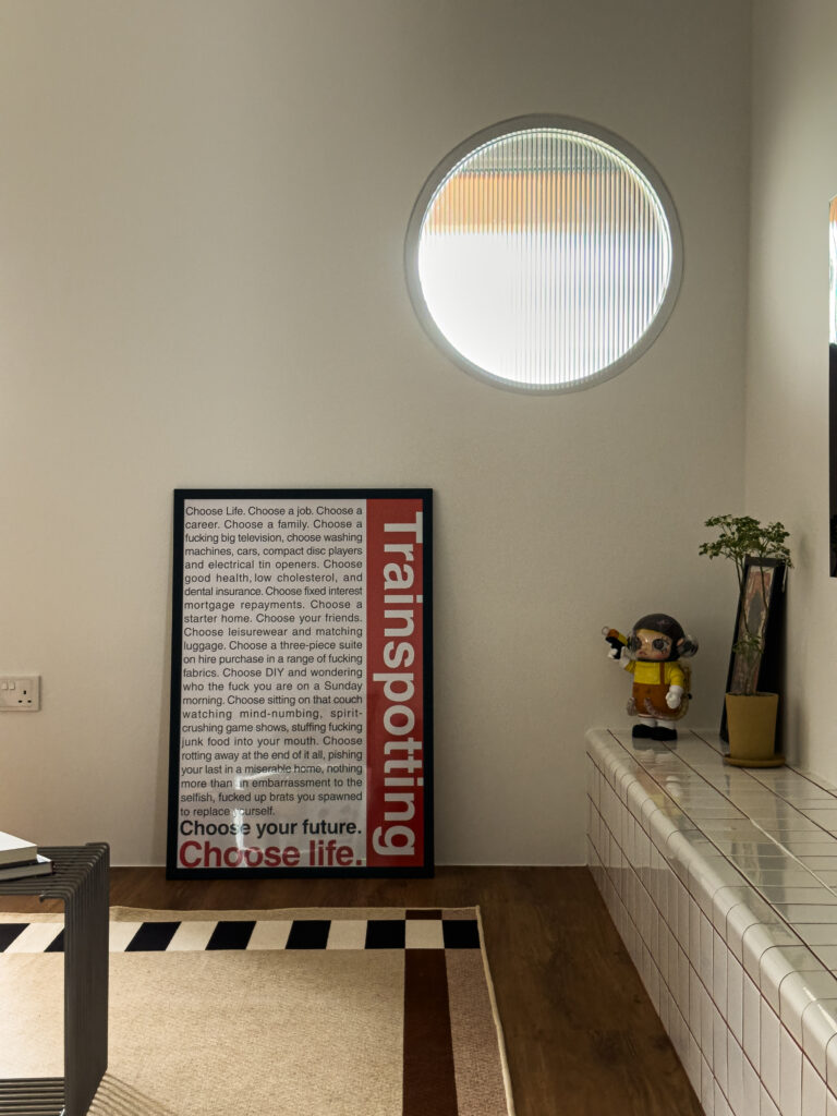 Feature corner with a round fluted glass window, a bold Trainspotting poster, and playful decor pieces adding character to the space.