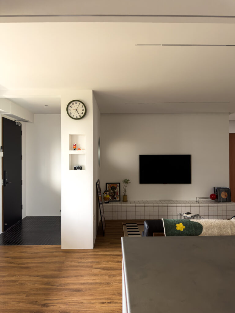 Living room view from the kitchen side, showing the tiled console against the wall, the round fluted window, and contrasting black mosaic entry floor.